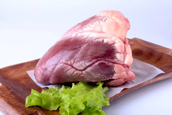 Rått nötkött hjärta och sallad blad på trä skrivbord isolerade på vit bakgrund från ovan och kopia utrymme. redo för matlagning. — Stockfoto