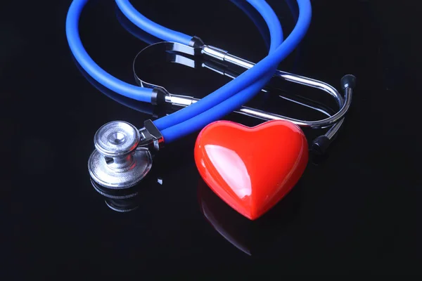 Stethoscope, Red heart and blood pressure meter on black mirror background. Selective focus. — Stock Photo, Image