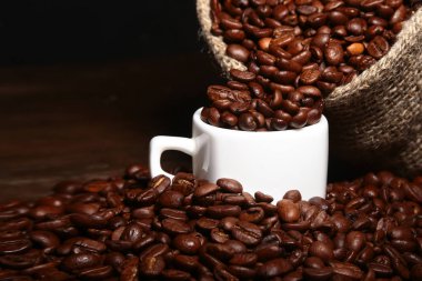 Taze kavrulmuş kahve çekirdekleri çuvala, kahve fincanı ve koyu arka plan üzerinde değirmeni