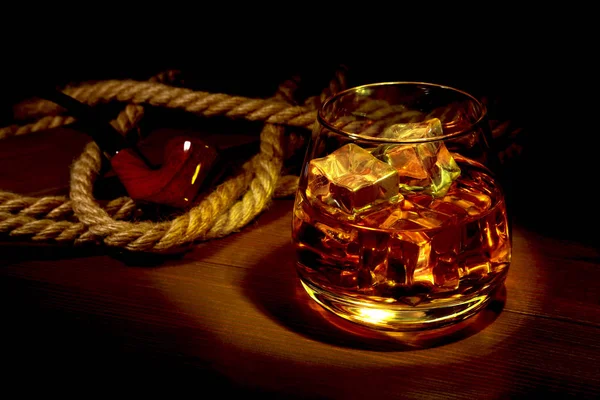 Glass of whiskey, cognac or brandy with ice and smoking pipe on wood table. Top view with copy space — Stock Photo, Image