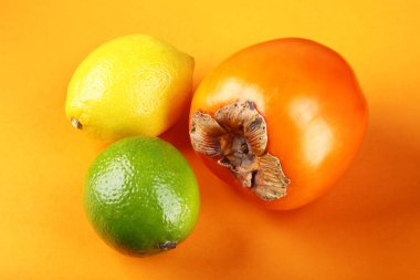 Taze karışık egzotik meyve limon, Trabzon hurması ve kireç turuncu bir arka plan üzerinde. Meyve arka plan. Üstten görünüm.