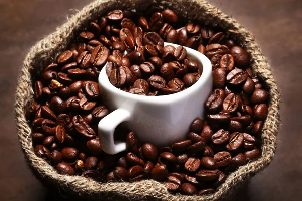 Frisch geröstete Kaffeebohnen in Klettenbeutel, Kaffeetasse und Mühle auf dunklem Hintergrund. — Stockfoto