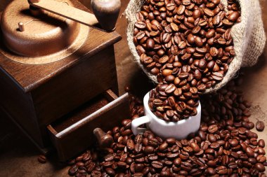 Taze kavrulmuş kahve çekirdekleri çuvala, kahve fincanı ve koyu arka plan üzerinde değirmeni.