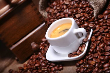 Taze kavrulmuş kahve çekirdekleri çuvala, espresso fincan ve taş zemin üzerine değirmeni.