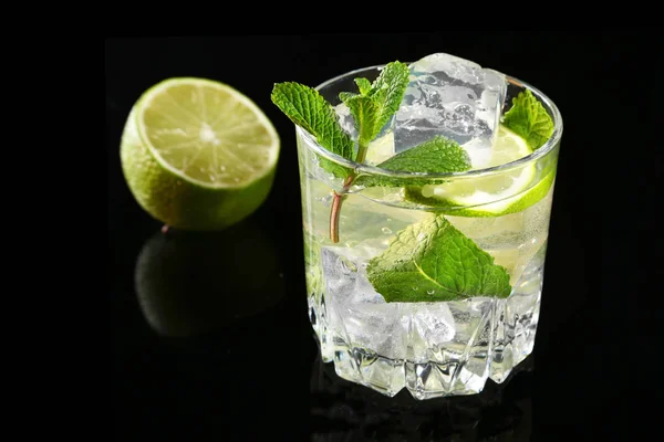 Glass of cocktail with rum, lime, ice cubes and mint leaves on black mirror background. — Stock Photo, Image