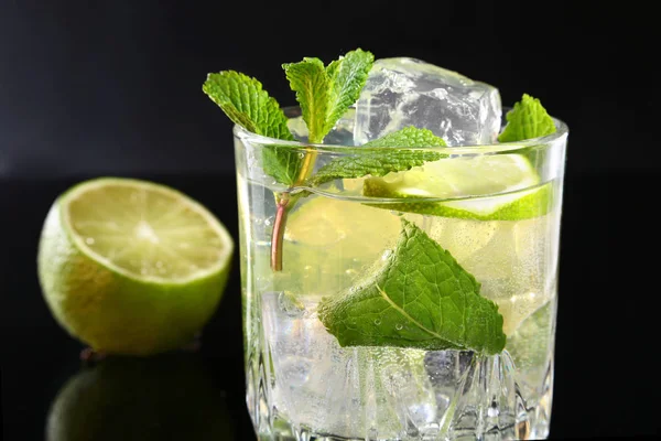 Glass of cocktail with rum, lime, ice cubes and mint leaves on black mirror background. — Stock Photo, Image