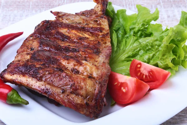 Revbensspjäll på barbeque och chilipeppar med tomat, salladsblad på vit platta — Stockfoto