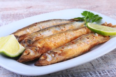 Küçük balık capelin ve beyaz tabakta dilimlenmiş limon kızartma derin. Bira için iyi snack.