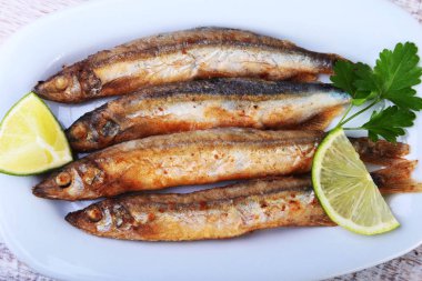 Küçük balık capelin ve beyaz tabakta dilimlenmiş limon kızartma derin. Bira için iyi snack.