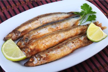 Küçük balık capelin ve beyaz tabakta dilimlenmiş limon kızartma derin. Bira için iyi snack.