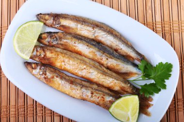 Küçük balık capelin ve beyaz tabakta dilimlenmiş limon kızartma derin. Bira için iyi snack.