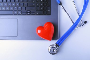 Doktor stetoskop, kırmızı kalp, dizüstü bilgisayar, rx reçeteli ve beyaz masa üstünde defter ile işyeri. Üstten Görünüm.