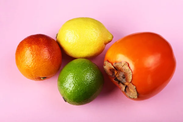 Verse gemengde exotische vruchten citroen, kaki en kalk op een roze achtergrond. Fruit de achtergrond. Bovenaanzicht. — Stockfoto