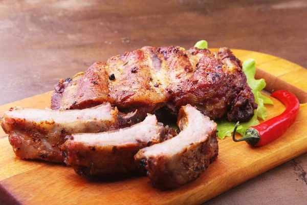 Gegrillte Rippchen vom Grill mit Salatblättern, scharfer Chilischote und Sauce auf Holzschneidebrett. — Stockfoto