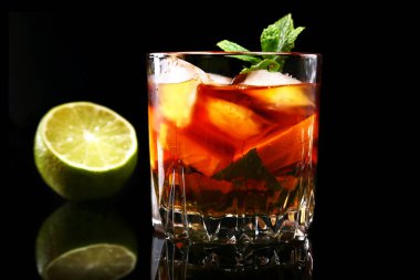 Siyah ayna arka plan üzerinde cam, koyu ROM ile kokteyl limon, portakal, buz küpleri ve nane yaprakları.