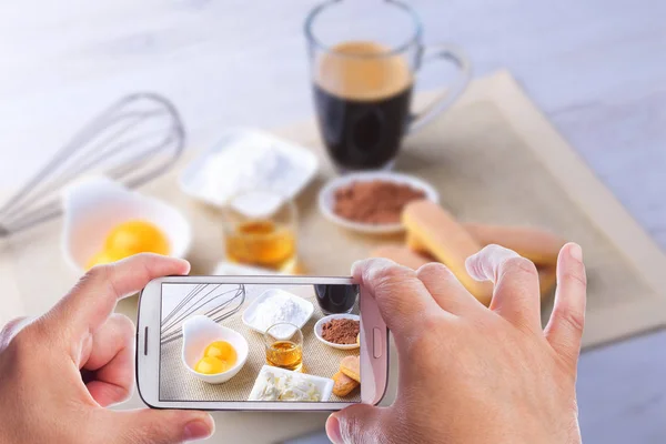 Manos del hombre con smartphone tomando foto ingrediente para pastel de tiramisú casero en primer plano. Vista superior . —  Fotos de Stock