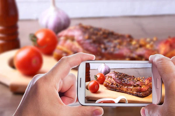 Manos del hombre con teléfono inteligente tomar foto Costillas de cerdo a la parrilla barbacoa Filete de striploin con salsa chimichurri y tomates en la tabla de cortar sobre fondo oscuro . —  Fotos de Stock