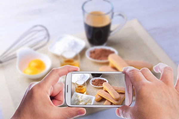 Manos del hombre con smartphone tomando foto ingrediente para pastel de tiramisú casero en primer plano. Vista superior . —  Fotos de Stock