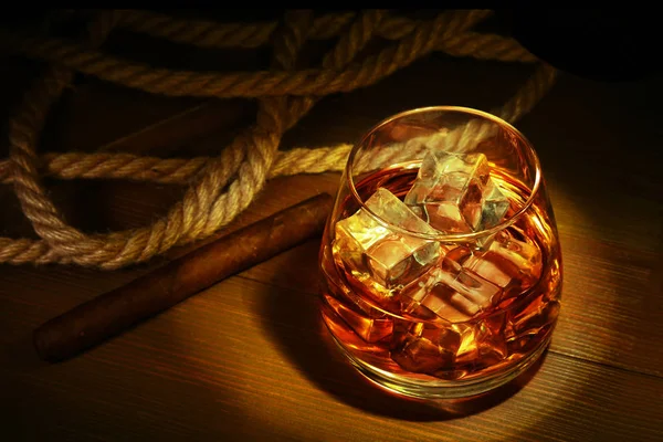 Glass with whiskey, ice cubes and smoking pipe on wooden background. — Stock Photo, Image