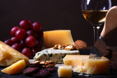 Çeşitli peynirler, fındık, üzüm, meyve, füme et ve servis masasında bir bardak şarap. Karanlık ve Moody tarzı. Metin için boş alan.