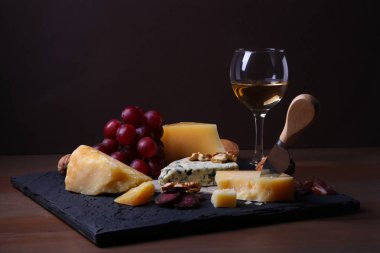 Assorted cheeses, nuts, grapes, fruits, smoked meat and a glass of wine on a serving table. Dark and Moody style. Free space for text. clipart