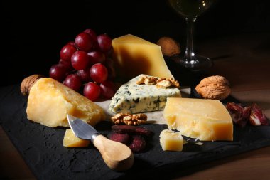 Çeşitli peynirler, fındık, üzüm, meyve, füme et ve servis masasında bir bardak şarap. Karanlık ve Moody tarzı. Metin için boş alan.