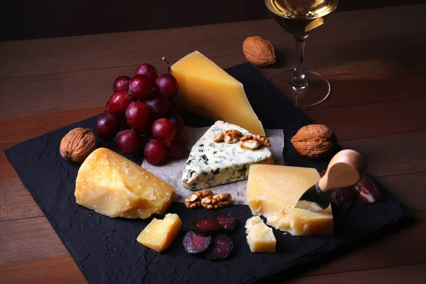 Käse, Nüsse, Trauben, Früchte, geräuchertes Fleisch und ein Glas Wein auf einem Serviertisch. dunkler und launischer Stil. Freiraum für Text. Stockbild