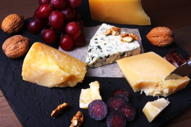 Çeşitli peynirler, fındık, üzüm, meyve, füme et ve servis masasında bir bardak şarap. Karanlık ve Moody tarzı. Metin için boş alan.