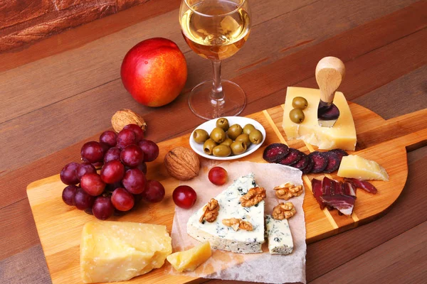 Výběr sýrů s ovoce, hrozny, ořechy a sýr nožem na dřevěný servírovací tác. — Stock fotografie