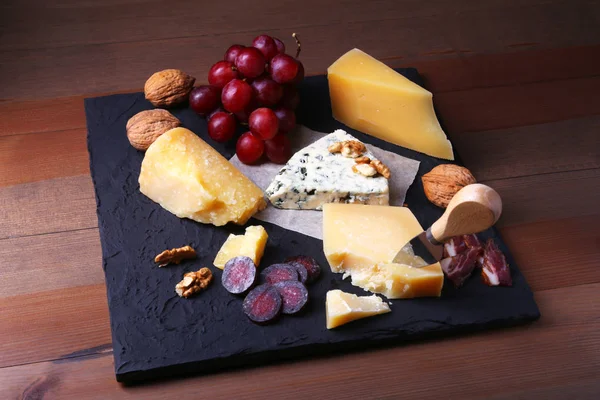 Výběr sýrů s ovoce, hrozny, ořechy a sýr nožem na dřevěný servírovací tác. — Stock fotografie