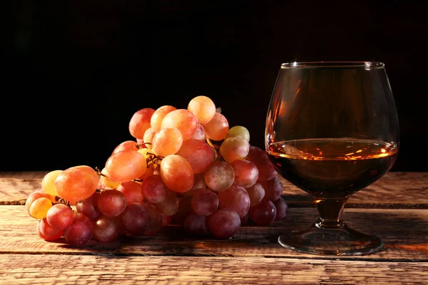 Cognac ou Brandy dans un verre et raisins frais, nature morte dans un style rustique, fond bois vintage, mise au point sélective . — Photo