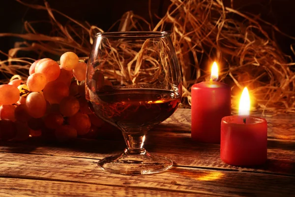 Verre avec cognac ou whisky, raisins et bougies de Noël sur fond de bois. Décoration de Noël . — Photo