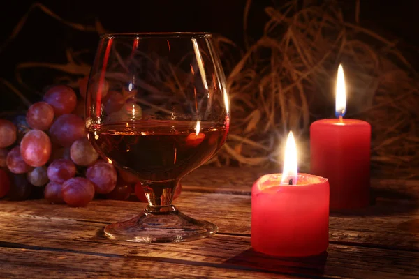 Glas med Cognac eller whisky, vindruvor och julljus på trä bakgrund. Juldekoration. — Stockfoto