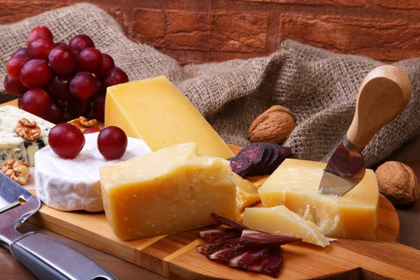 Ассортимент сыра с фруктами, виноградом, орехами и сырным ножом на подносе . — стоковое фото