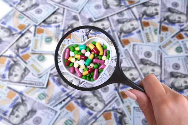 Konzept der Krankenversicherung. Pillen in der Lupe vor dem Hintergrund vieler Dollarnoten — Stockfoto