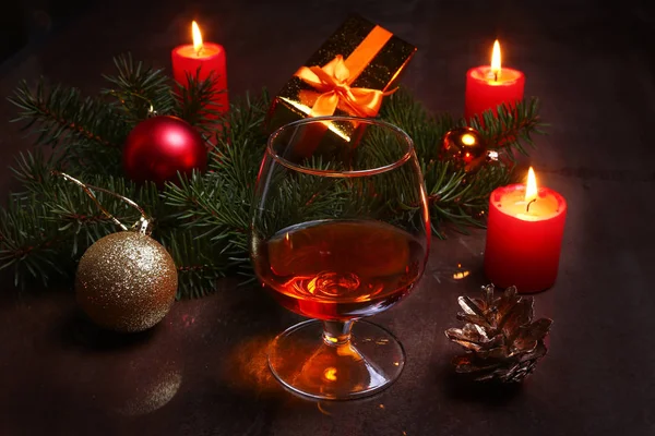 Weihnachtsdekoration mit einem Glas Cognac oder Whiskey, roten Kerzen, Geschenkbox und Weihnachtsbaum. Selektiver Fokus. — Stockfoto