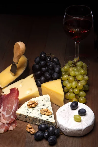 Käse, Nüsse, Trauben, Früchte, geräuchertes Fleisch und ein Glas Wein auf einem Serviertisch. dunkler und launischer Stil. Freiraum für Text. lizenzfreie Stockfotos