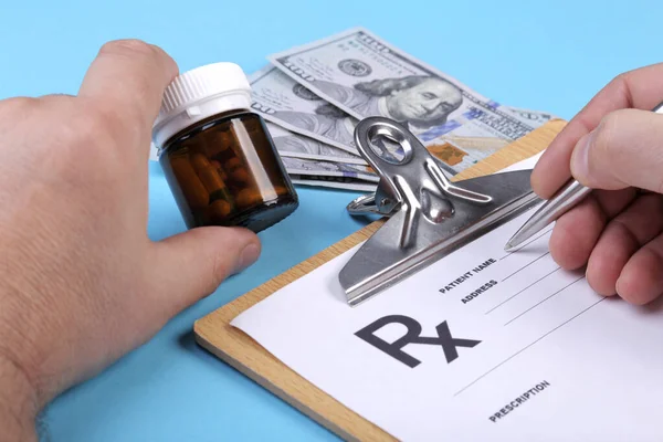 Médico ou farmacêutico masculino segurando frasco ou frasco de pílulas na mão em um fundo de notas de dólares e escrevendo prescrição em um formulário especial. custos médicos e conceito de pagamento de cuidados de saúde . — Fotografia de Stock