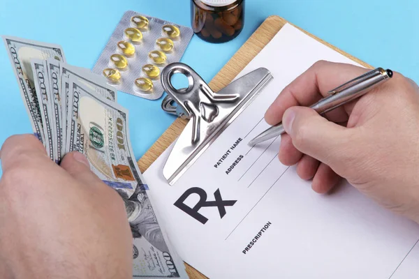 Médico masculino ou farmacêutico segurando dinheiro na mão e escrevendo prescrição em um formulário especial. custos médicos e conceito de pagamento de cuidados de saúde . — Fotografia de Stock