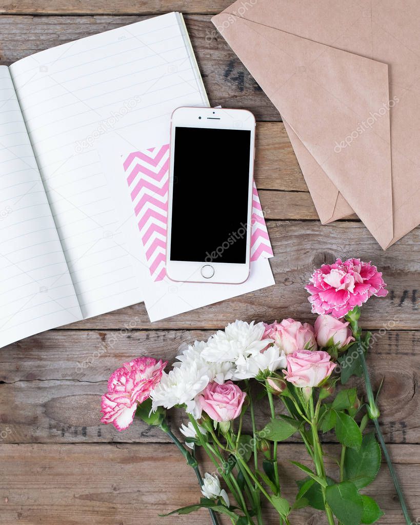 Phone with paper and beautiful flowers on wooden table