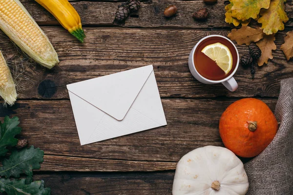Autumn mood: letter , tea, pumpkins and corn with yellow leaves on a wooden background