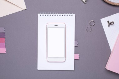 Gri arkaplan görünümlü beyaz not defteri ve nakışlı boş ekranlı cep telefonu