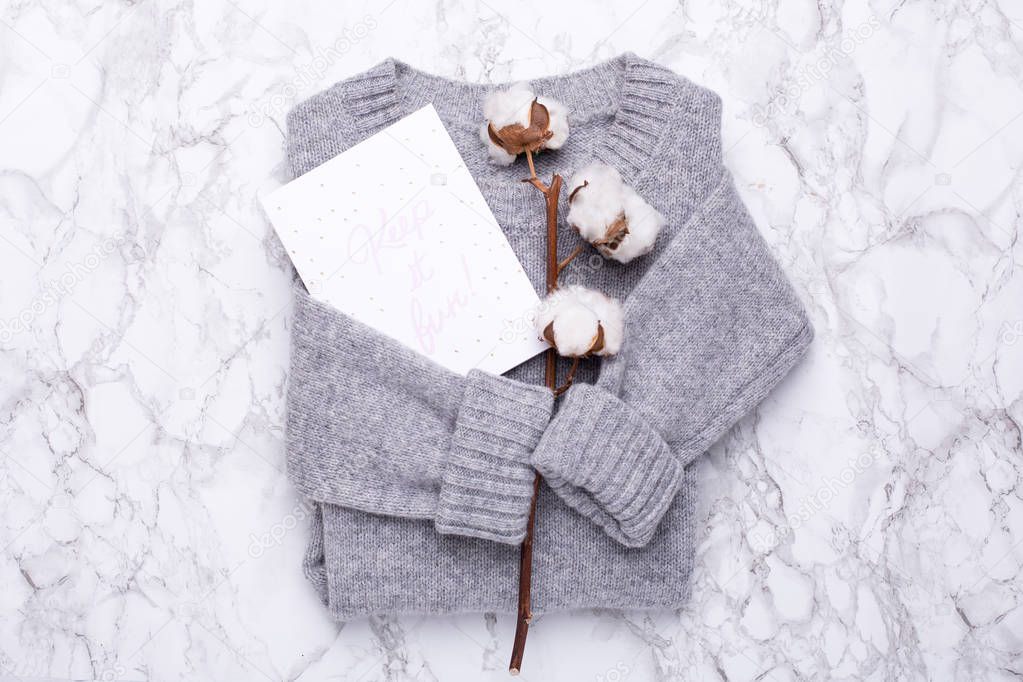 Cozy gray sweater with a postcard and cotton on a marble background top view