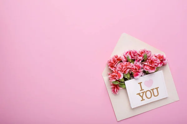 An envelope with pink flowers and a card I love you on a pink background top view