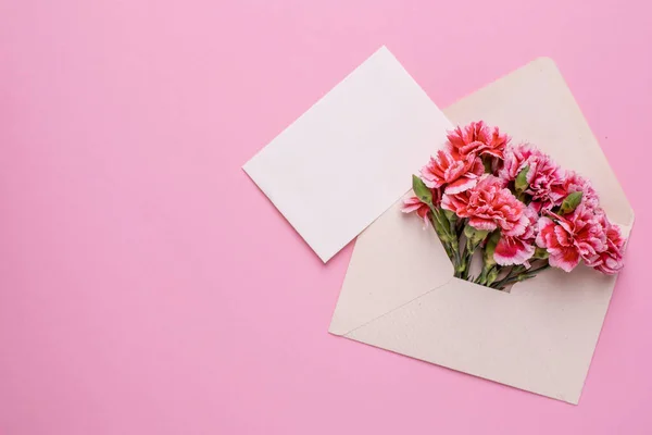 An envelope with pink flowers and a present card on a pink background top view