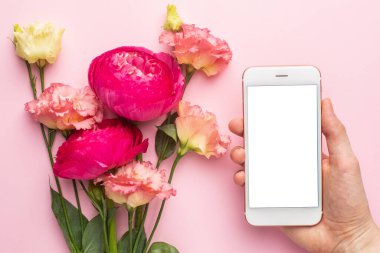 Cep telefonu ve pembe çiçek buketi pastel arka plan görünümünde.