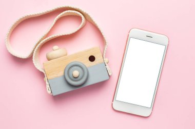 Cep telefonu ve pembe arka planda tahta oyuncak kamera, doğal ekolojik materyal ve erken bebek gelişimi.
