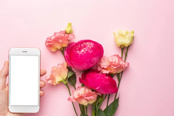 Cep telefonu ve pembe arkaplanlı Ranunculi çiçek buketi.