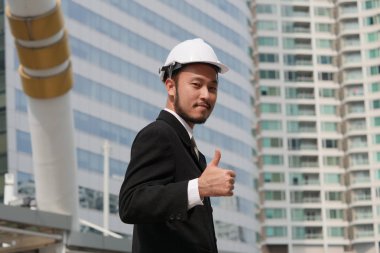 Buliding site üzerinden samrt mühendislik ayakta ve başparmak yukarıya, mutlu ekip çalışması kavramı gösterilen.