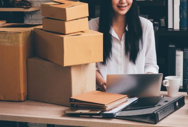 Pacel kutuları arka plan ile dizüstü bilgisayar kullanarak çalışan Asain kadın.